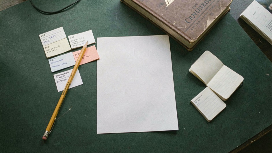 Overhead documentary photograph of index cards, a pencil, a book and a small notebook on a deep green desk, blank paper with no legible writing, soft window light. Distinct supporting card P007 2 composition for this editorial entry.