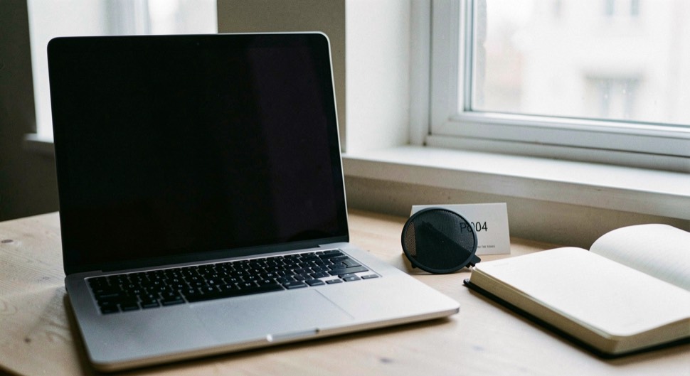 Documentary photograph of a laptop with a completely blank dark screen beside a notebook, a small privacy shutter and a window reflection, no readable interface, cool morning light. Distinct supporting card P004 1 composition for this editorial entry.