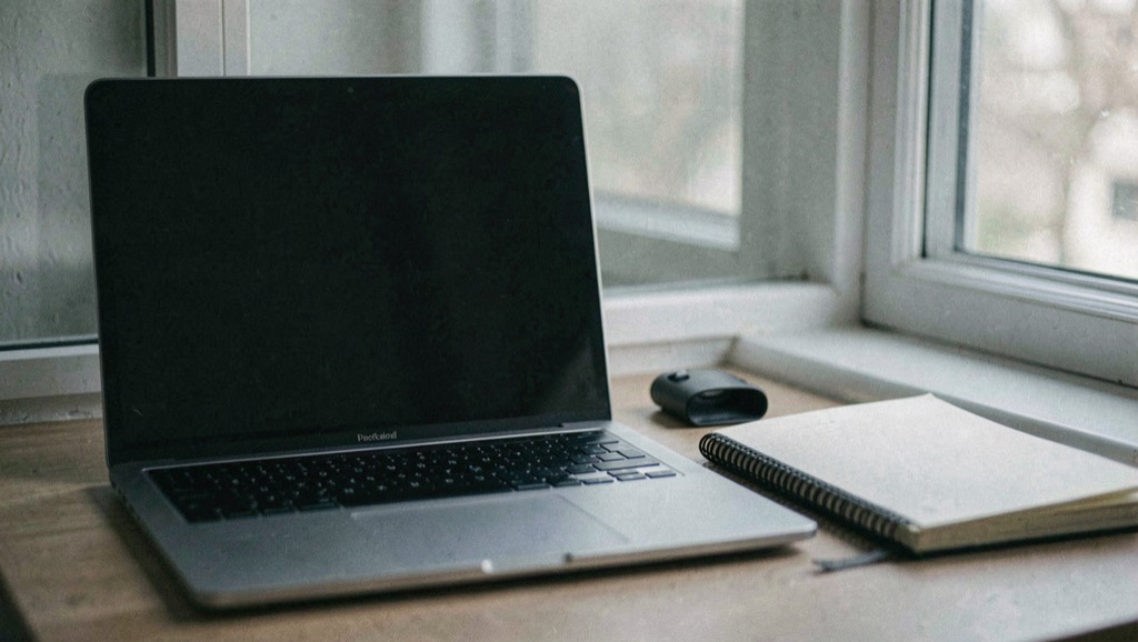 Documentary photograph of a laptop with a completely blank dark screen beside a notebook, a small privacy shutter and a window reflection, no readable interface, cool morning light. Distinct supporting card P109 2 composition for this editorial entry.