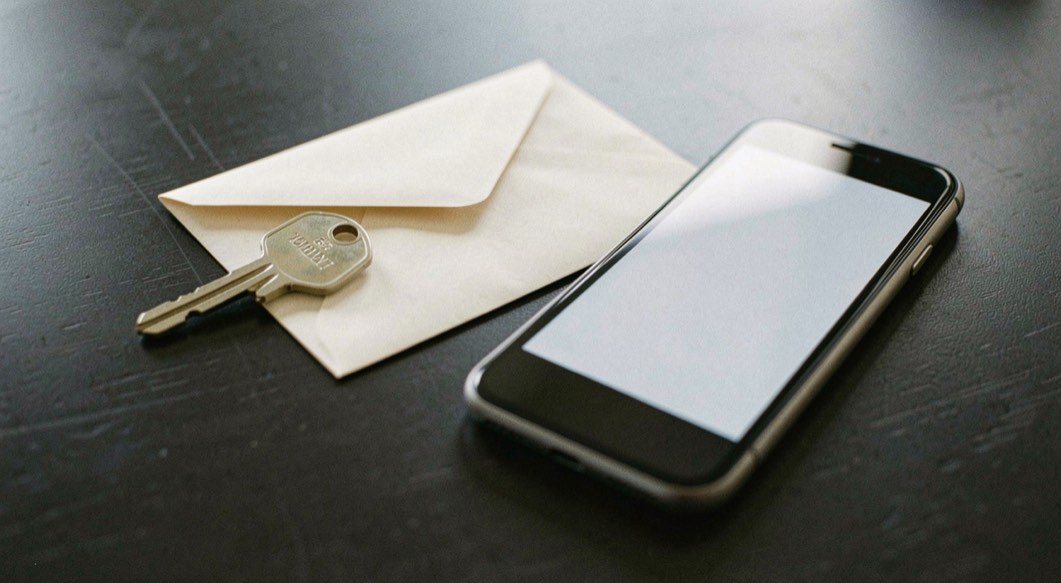 Documentary photograph of a spare security key, a sealed envelope and a phone with a blank screen on a dark table, no readable text, careful side light. Distinct supporting card P109 3 composition for this editorial entry.